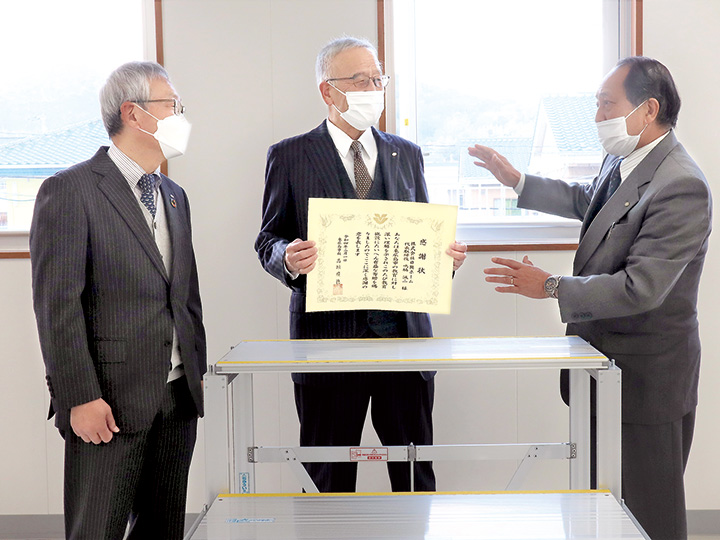 寄贈したひな壇の前で談笑する（左から）鳴脇社長、村尾会長、津森教育長（撮影・山北）