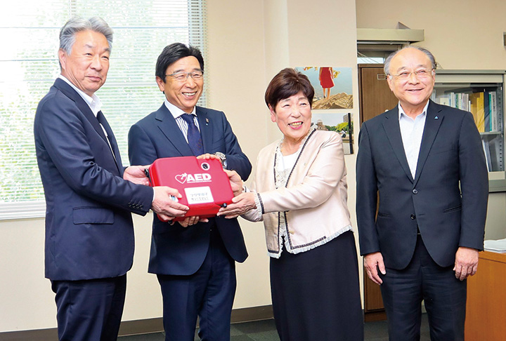 寄贈したAEDを手に記念撮影する（左から）市場教育長、上垣会長、三宅副会長、法人会の山下勇治副会長（撮影・山北）