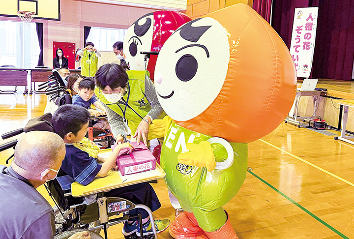 人権イメージキャラクターの「人KENまもる君」から花の種を受け取る児童（撮影・久野）