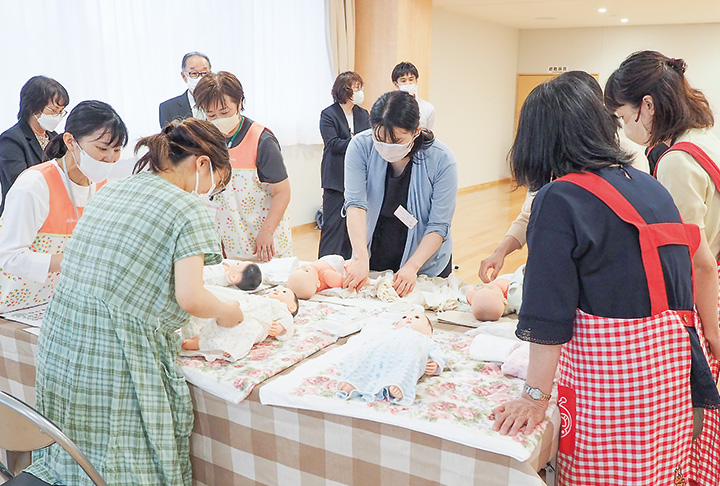 赤ちゃんの人形を使ったお世話体験。服の着替えに挑戦する妊娠中の参加者（撮影・原田）