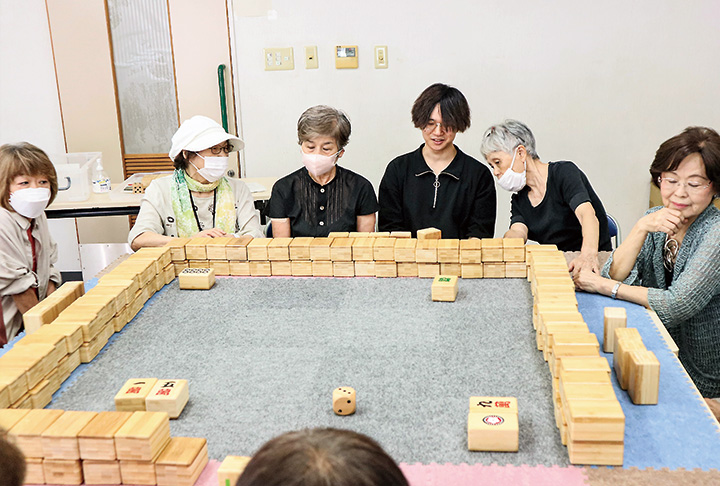 サロン参加者と一緒にコミュニケーション麻雀を楽しみながら取材する学生（右から3人目）（撮影・山北）