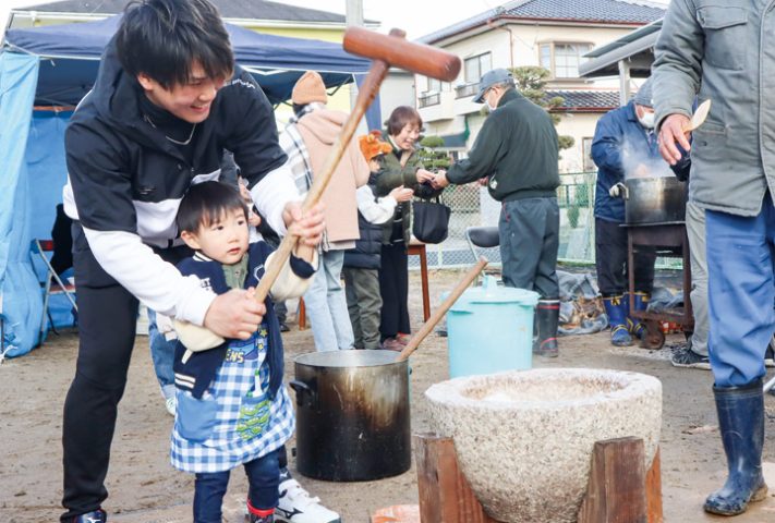 保護者と一緒にきねを振り上げ餅つきを楽しむ子ども（撮影・山北）