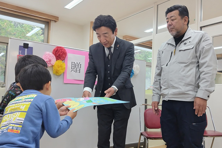 園児から絵をプレゼントされ笑顔の上垣会長（中央）と木村理事