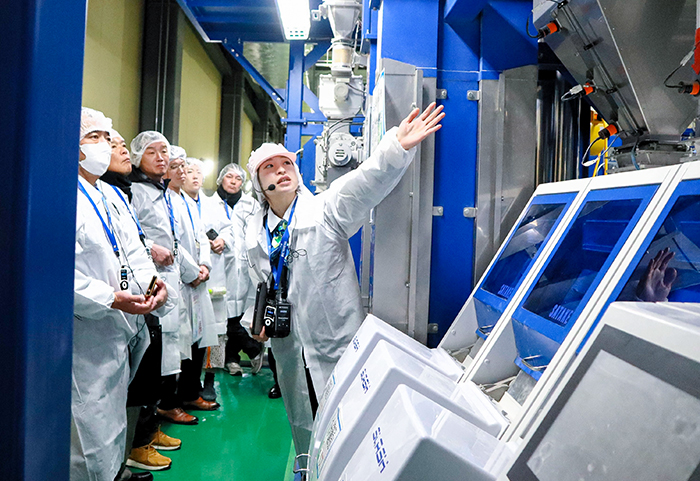 担当者(右)の説明を聞きながら工場見学をする生産者ら(撮影・山北)