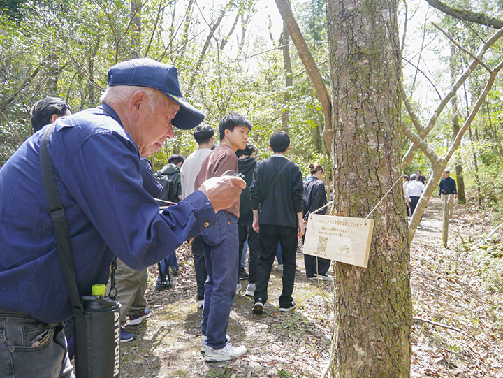 樹木に設置された二次元コードを飲み込んで情報をチェックする参加者(撮影・児玉)