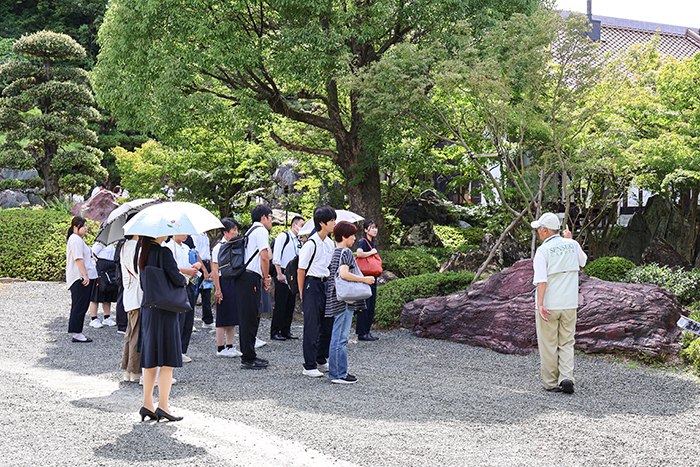 ガイドさんに案内され、庭園内散策やタイムカプセル収納庫の撮影などを楽しむ参加者（撮影・𦚰）