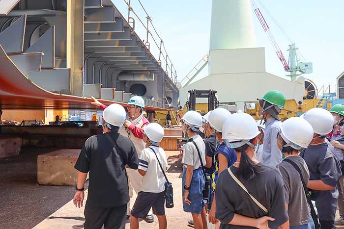 船体の建造工程について関心を持ち、山野副工場長（奥）の説明に耳を傾ける子どもら