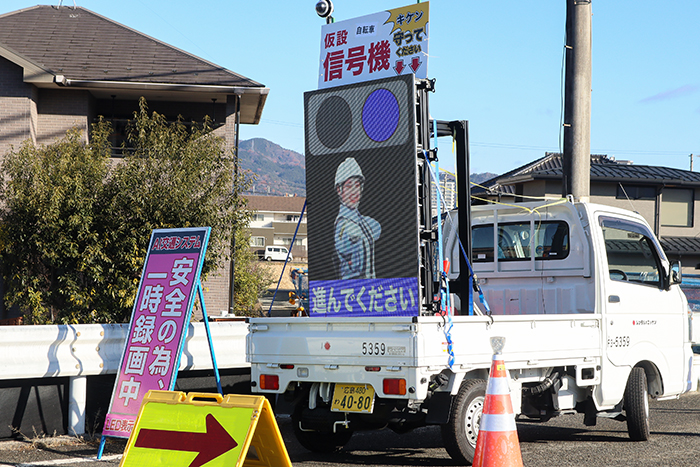 ＬＥＤ看板は「止まれ」と「進め」の各表示を交互に切り替え、通行車両や二輪車、歩行者を警備員の映像で表示しリアルに誘導（撮影・山北）
